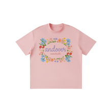Load image into Gallery viewer, A light pink short-sleeve crewneck t-shirt featuring a colorful floral wreath graphic on the chest with the text 'andover massachusetts' in purple and pink script.