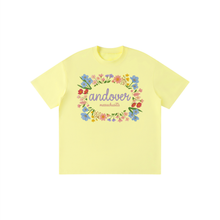 Load image into Gallery viewer, A pale yellow short-sleeve t-shirt with a colorful floral wreath graphic on the chest containing the text 'andover massachusetts'.
